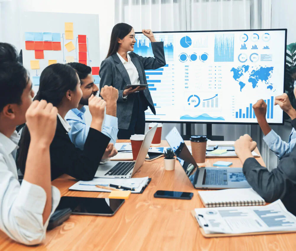 Business people celebrate after successful presentation or meeting on data analysis display on TV screen. Happy team gathers in office room, cheer to collaboration with celebratory gesture. Concord